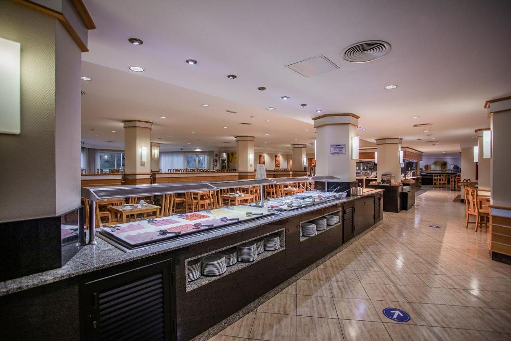 Restorāna interjers ar bufetes zonu un koka galdiem, piedāvājot plašu izvēli ēdieniem un komfortablu atmosfēru.