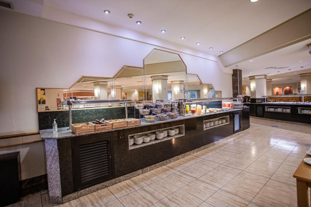 Pusdienu bufete ar dažādiem ēdieniem un dzērieniem, iekārtota modernā vidē ar spoguļiem un apgaismojumu.