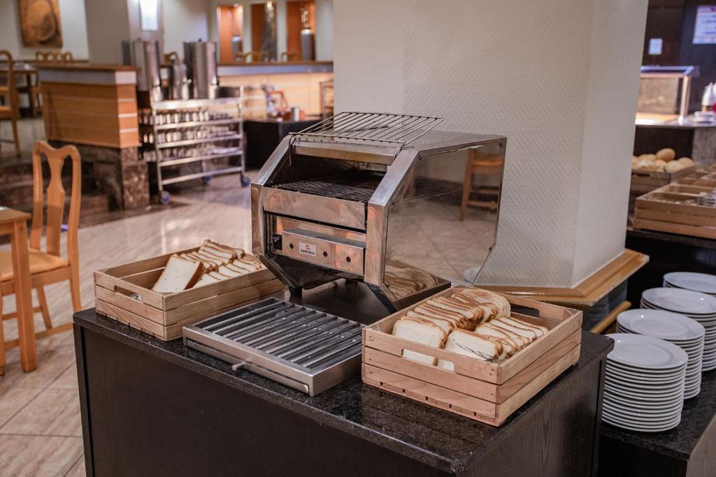 Sviestmaizes grauzdētājs ar maizes šķēlēm, izvietots restorānā, ar redzamu interjeru un galdiem fonā.