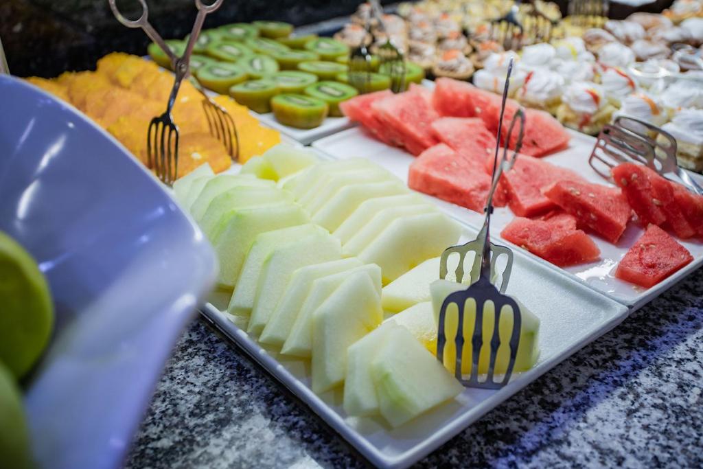 Svaigi griezti augļi, tostarp melone, arbūzs un kivi, sakārtoti uz galda ar metāla šķērēm. Ideāli piemērots veselīgai uzkodu izvēlei.