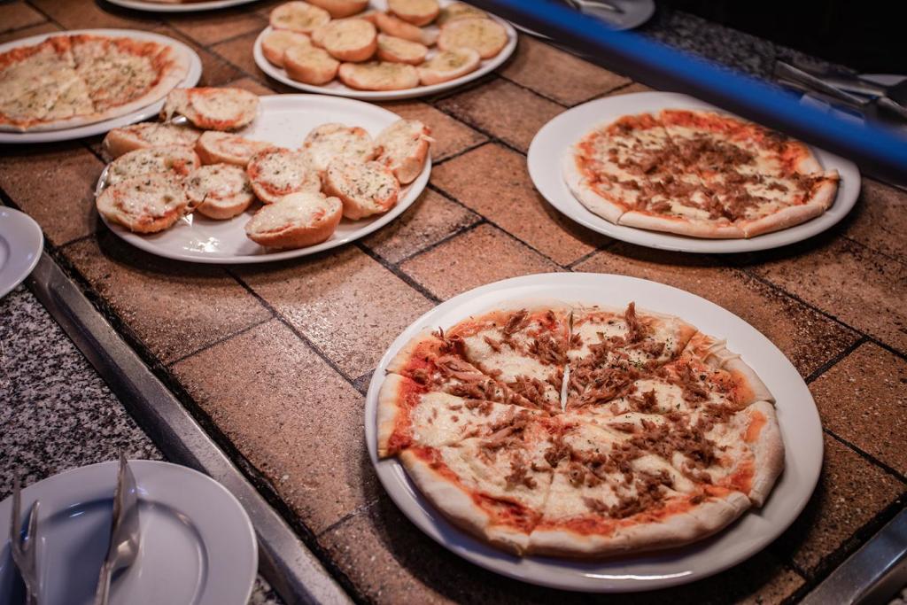 Pica un ceptas maizītes uz šķīvjiem, izkārtotas uz galda. Redzami dažādi picas varianti ar gaļu un sieru.