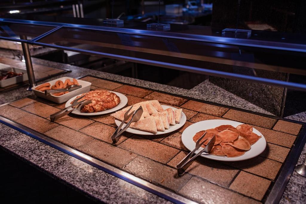 Svaigu ēdienu bufete ar dažādām uzkodām, tostarp pīrāgiem, pankūkām un desām, servēta uz akmens galda.