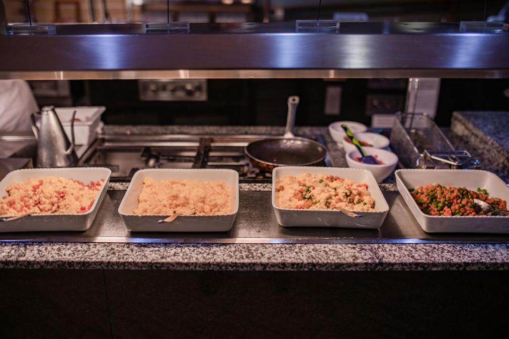 Gatavošanas zona ar vairākām traukos pasniegtām ēdienu porcijām, tostarp graudaugiem un dārzeņiem.