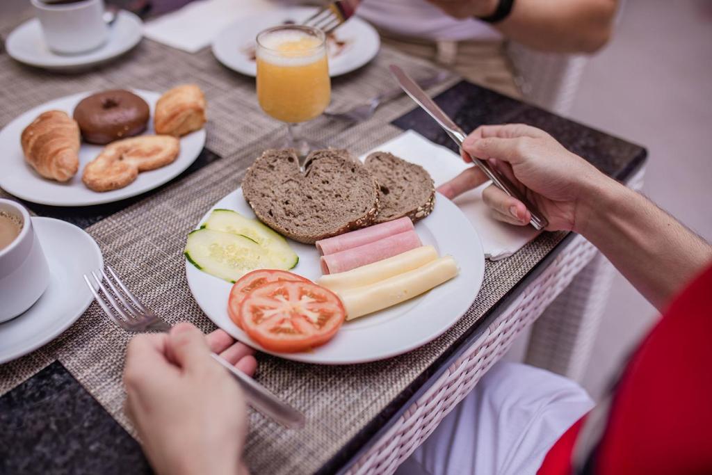 Brokaļa plate ar maizi, šķiņķi, sieru, tomātiem un gurķiem, papildināta ar kafiju un saldām uzkodām, piemēram, kruasāniem un dzērieniem.