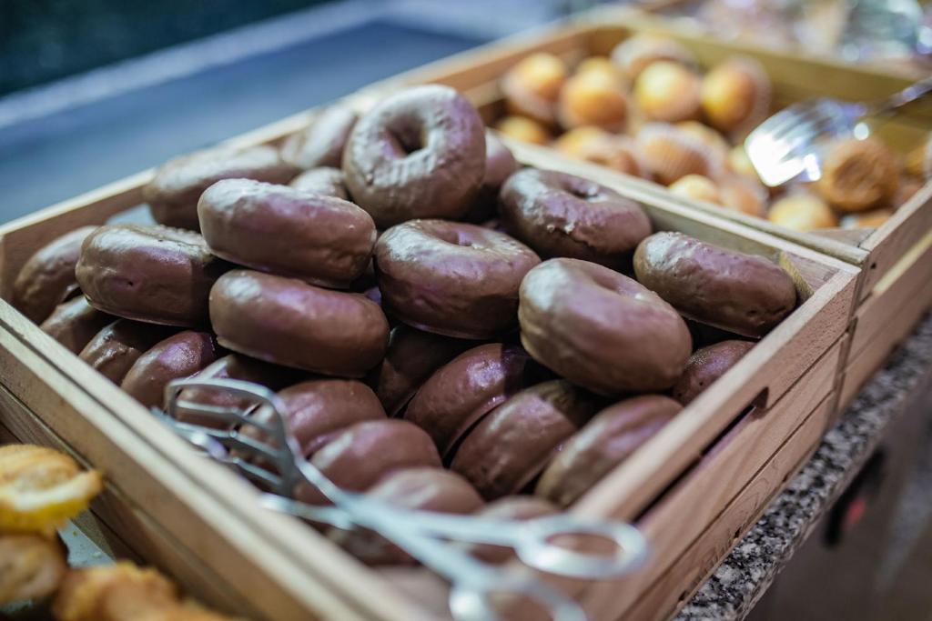 Šokolādes glazētie donati sakrauti koka kastē, blakus citiem saldumiem. Ideāli piemēroti gardēžiem.