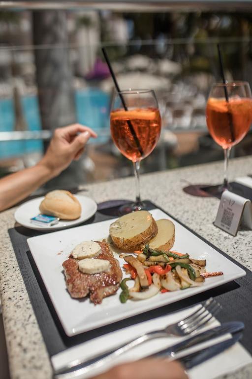Delicious steak served with grilled vegetables and a baked potato, accompanied by refreshing cocktails on a sunny terrace.