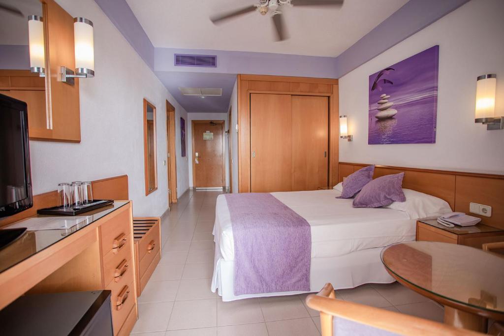 Mūsdienīgs viesnīcas numurs ar gaisīgu interjeru un harmonisku krāsu paleti, kas ietver violetas akcentus un koka mēbeles. Numurā ir ērtā gulta, galds un televizors, radot patīkamu atmosfēru atpūtai.