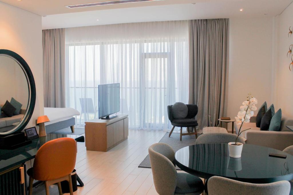 Mūsdienīga viesnīcas numura interjers ar plašu telpu, mēbelēm un apgaismojumu, kas rada komfortablu atmosfēru. Logi ar gaisīgiem aizkariem piedāvā skatu uz āru.