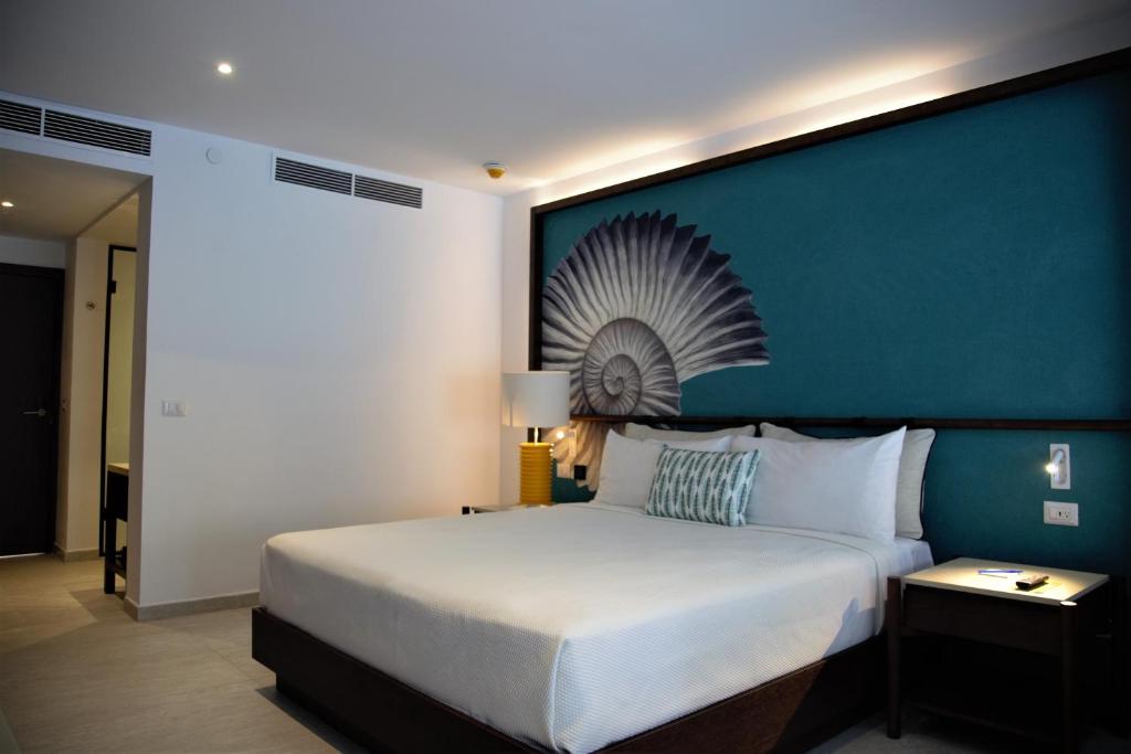 Mūsdienīgs viesnīcas numurs ar plašu gultu un dekoratīvu akcentu uz sienas. Telpā ir moderns apgaismojums un eleganta mēbelēšana, radot komfortablu atmosfēru.