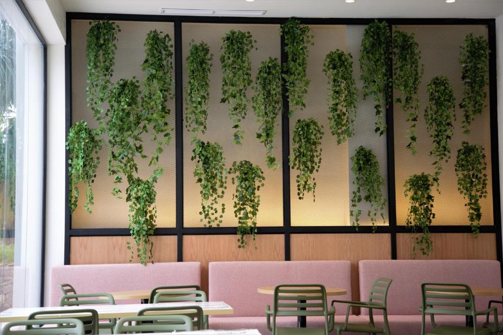 Mūsdienīgs interjers ar vertikālām augu kompozīcijām uz sienas, kas rada patīkamu atmosfēru. Sēdvietas ar rozā un zaļām krāsām papildina telpas dizainu.