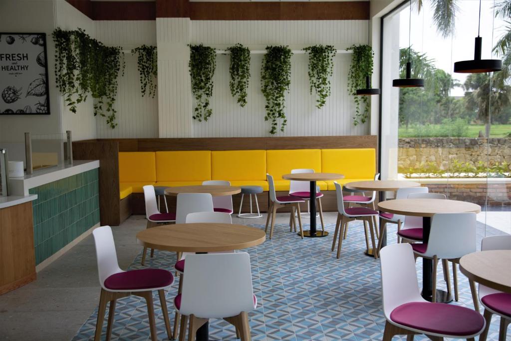 Mūsdienīga kafejnīca ar gaišām krāsām, stilīgām mēbelēm un zaļām augu kompozīcijām. Telpas dizains rada patīkamu un relaksējošu atmosfēru.