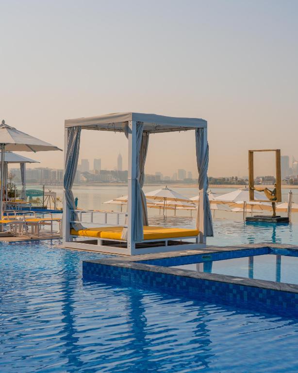 Peldbaseins ar saulainu atpūtas zonu un modernu pilsētas ainavu fonā, radot relaksējošu atmosfēru. Ideāls skats uz ūdeni un mīkstiem dīvāniem.