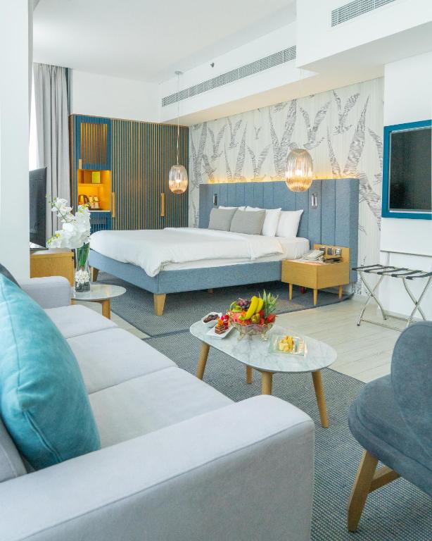 Mūsdienīgi iekārtota viesnīcas numura interjers ar ērtu gultu, dīvānu un elegantu galdniecību, kurā redzami augļi un uzkodas. Numurs ir apgaismots ar stilīgām lampām un rotāts ar modernu sienu apdari.