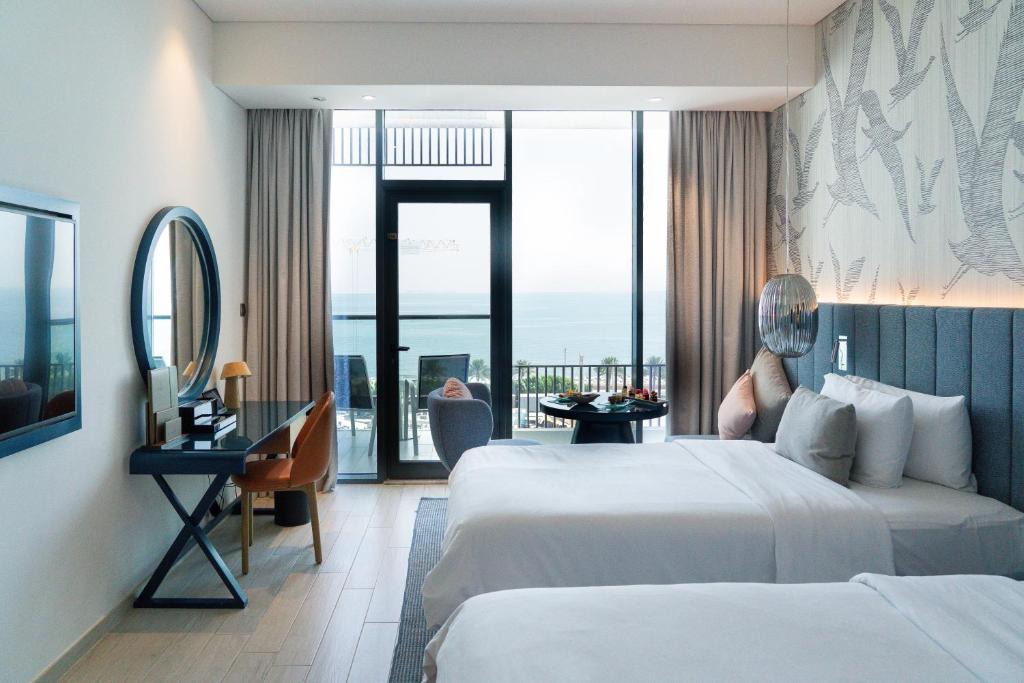 Moderns viesnīcas numurs ar divām gultām, skatu uz jūru un ērtu darba galdu. Interjers ir gaišs un elegants, radot relaksējošu atmosfēru.