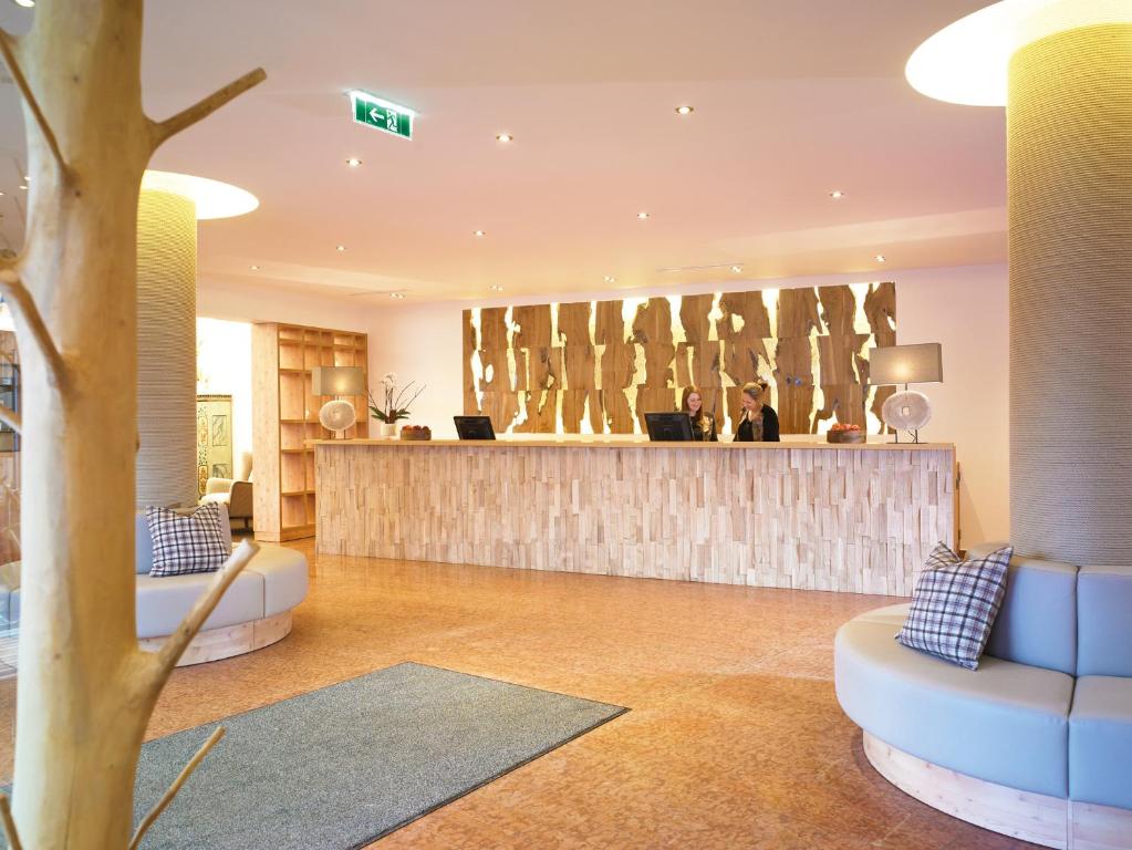 Mūsdienīgs viesnīcas reģistratūras interjers ar koka akcentiem un ērtām sēdvietām. Apkalpojošais personāls smaidīgi pieņem viesus pie stūra letes.