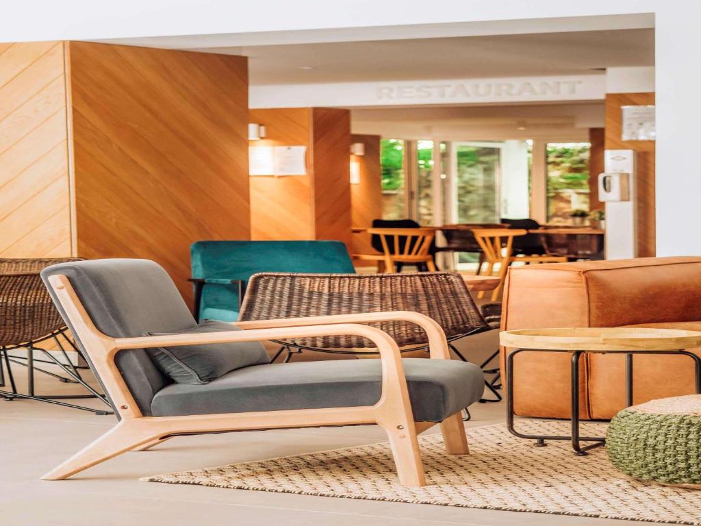 Mūsdienīgs viesnīcas interjers ar ērtu krēslu, koka mēbelēm un viesnīcas restorāna zīmi. Telpā ir dažādas sēdvietas un dekoratīvi elementi, kas rada viesmīlīgu atmosfēru.