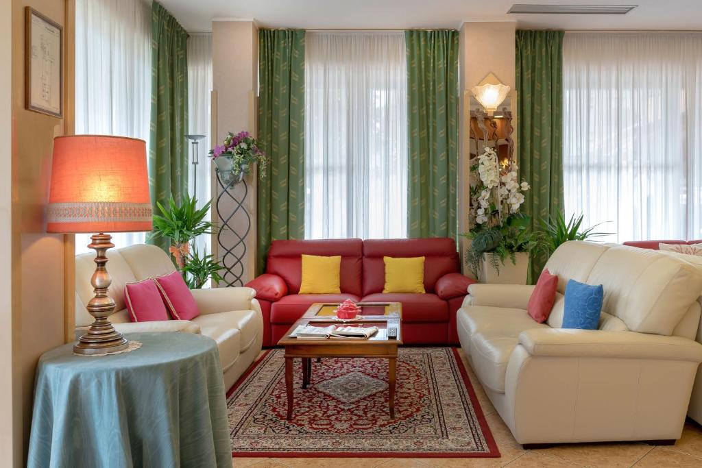 Mūsdienīgs viesistabas interjers ar sarkaniem un baltajiem dīvāniem, kas papildināti ar spilveniem, un elegantu galdiņu. Telpa ir gaiša un ērta, ar zaļiem aizkariem un dekoratīvām augu kompozīcijām.