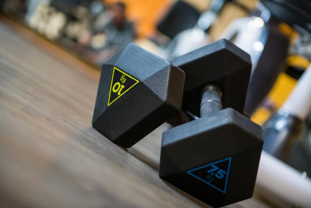 Svara hanteles ar 7,5 kg un 10 kg svaru, novietotas uz grīdas, sporta zālē. Ideāla izvēle treniņiem un muskuļu stiprināšanai.