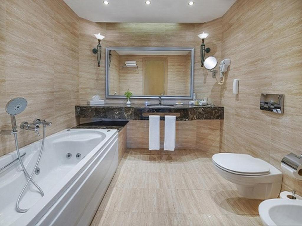 Mūsdienīga vannas istaba ar baltu vannu, melnu marmora virsmu un spoguli, kas atspoguļo elegantu dizainu un patīkamu apgaismojumu.