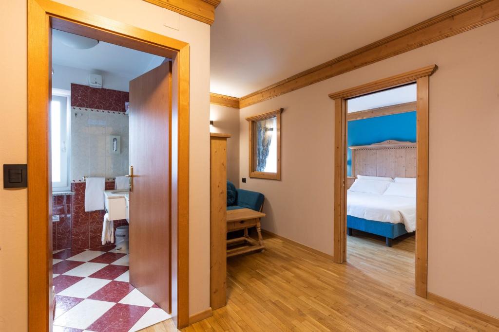 Mūsdienīgs viesnīcas numura interjers ar koka apdari, redzami divi numuri - guļamistaba ar zilu sienu un vannas istaba ar sarkanu flīžu grīdu.