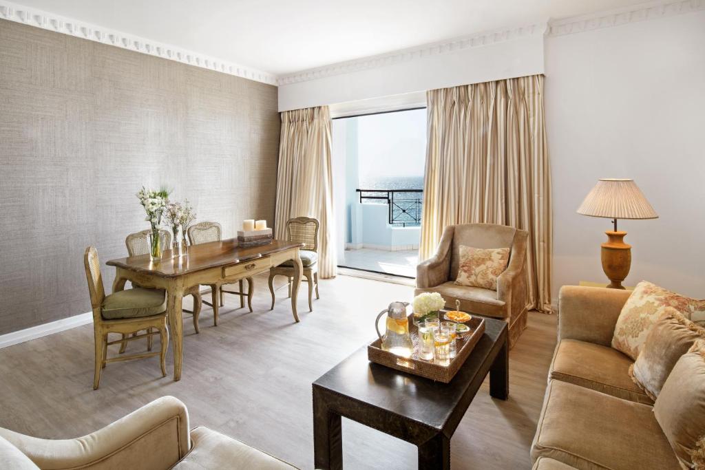 Gaisma un moderns viesistabas interjers ar koka galdu, ērtām mēbelēm un skatu uz jūru. Interjers ir elegants un mājīgs, ar dabīgām krāsām un ziediem uz galda.