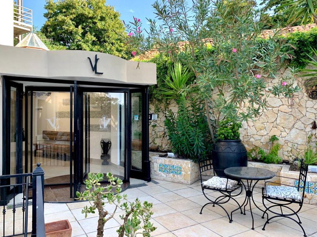 Ieejas zona ar rotējošām durvīm un elegantu augu noformējumu, radot patīkamu atmosfēru. Apkārt esošās terases mēbeles un dārzs piešķir vietai viesmīlību.