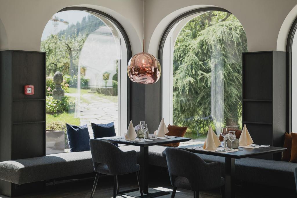 Moderns restorāna interjers ar elegantiem galdiem un komfortablām mēbelēm, caur lieliem logiem redzams dārzs. Centra gaismas avots piešķir siltumu un stilīgu atmosfēru.