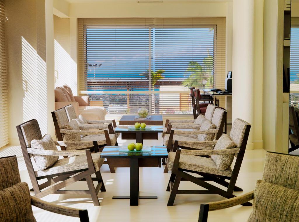 Mūsdienīgs un gaišs dzīvojamās telpas interjers ar komfortablām krēslām un galdiem, kas nodrošina skatu uz jūru. Telpā ir gaismas spēle un siltas krāsas, radot relaksējošu atmosfēru.