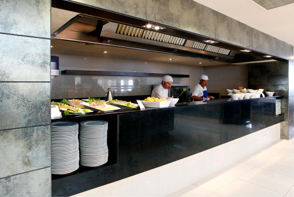 Restorāna virtuve ar diviem šefpavāriem, kas strādā pie bufetes. Uz galda redzami dažādi ēdieni un trauki.