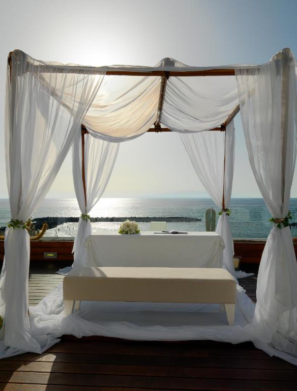 Romantiska kāzu ceremonijas vieta ar baltām drānām un skaistu jūras skatu, kas rada burvīgu atmosfēru.