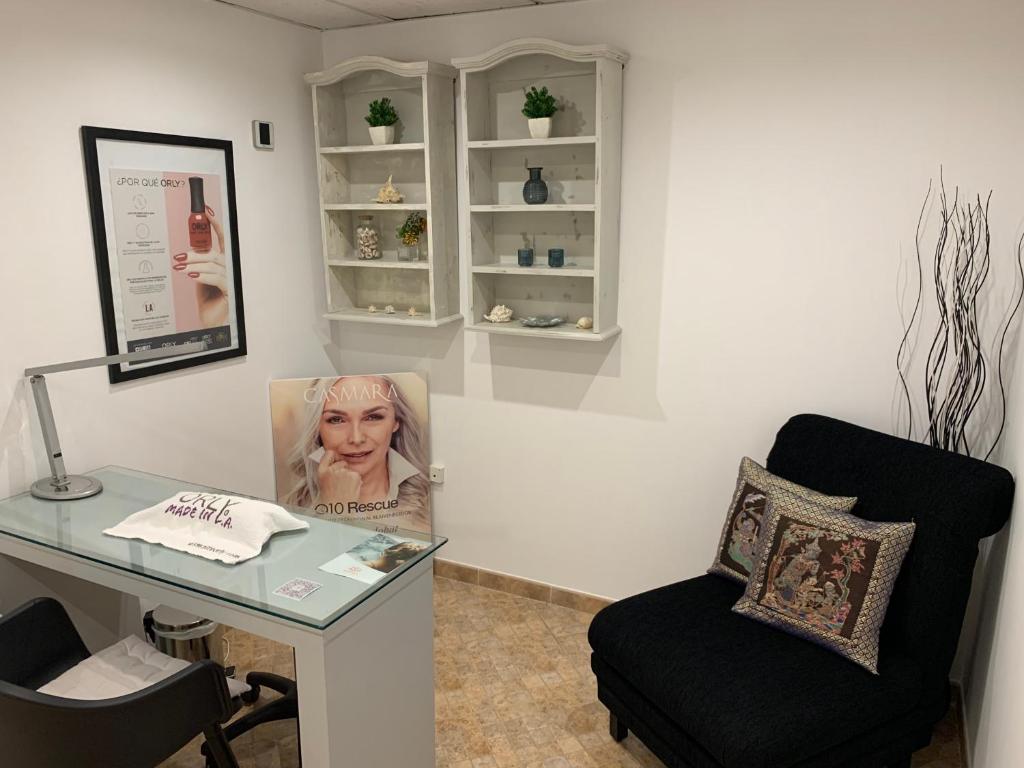 Mūsdienīga estētikas kabinets ar elegantu galdu, ērtu krēslu un dekoratīvām plauktiem, kas satur greznus aksesuārus un augu elementus. Uz galda atrodas izstrādājumi un reklāma par kosmētikas zīmolu.