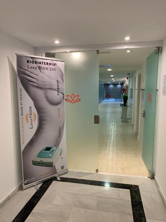 Ieeja uz estētisko centru ar reklāmas stendu par biodiatermiju, kas norāda uz LavaTRON 250 ierīci. Apskatāma gaiša telpa ar flīzēm un dekoratīvu elementu.