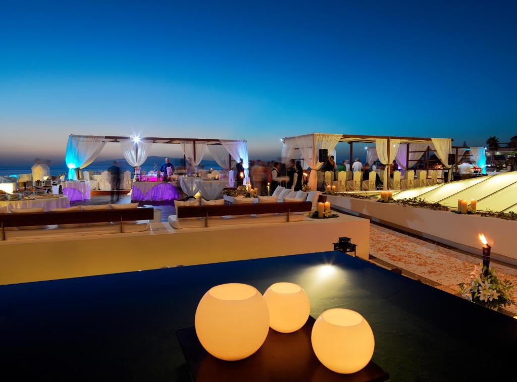 Romantiska vakara atmosfēra uz jumta terases ar apgaismotām galdiem un dekorācijām, kas izceļ jūras ainavu saulrieta gaismā.