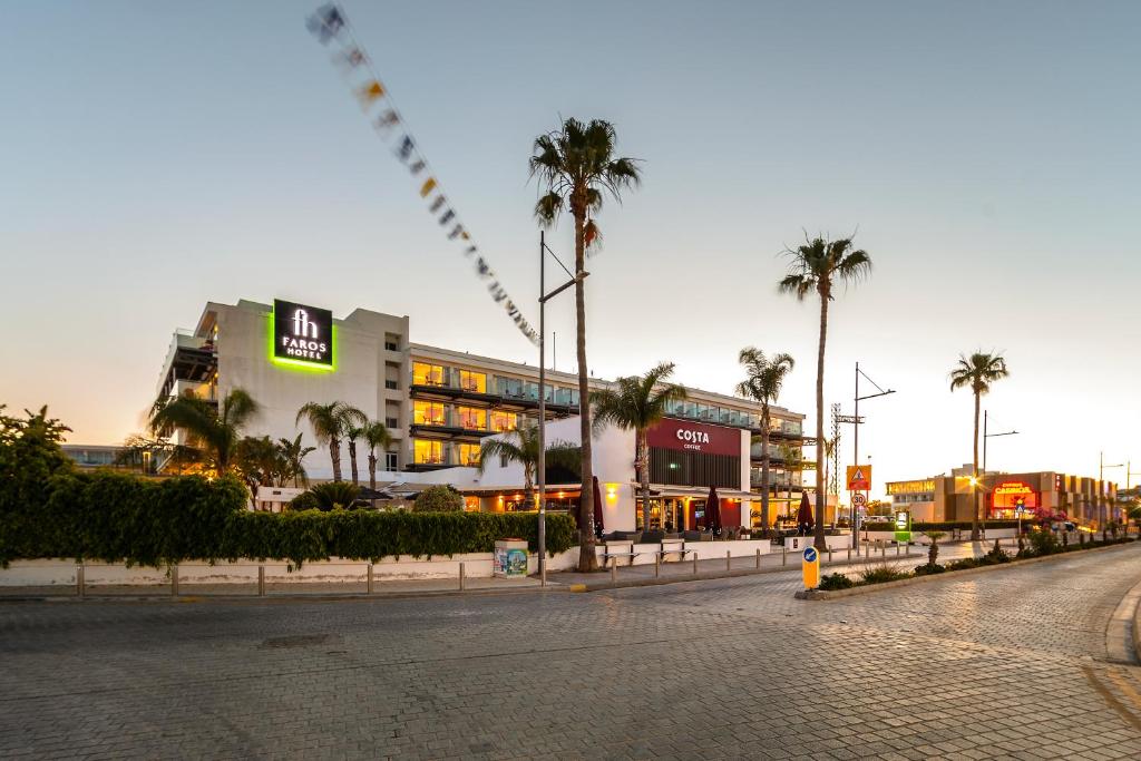 FAROS viesnīcas un Costa kafijas veikala skats pie saulrieta, apzaļumoti koki un iela ar bruģi.