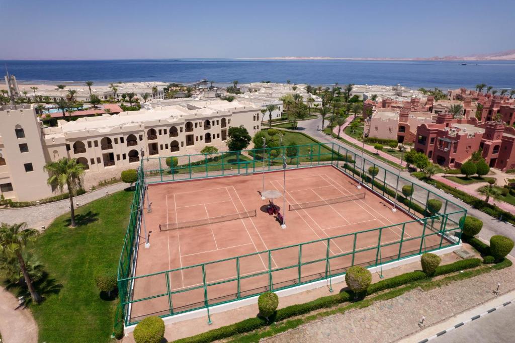 Tenisa laukums ar skatu uz jūru, apkārt esošās ēkas un zaļš ainavu dizains. Ideāla vieta atpūtai un sportiskām aktivitātēm.