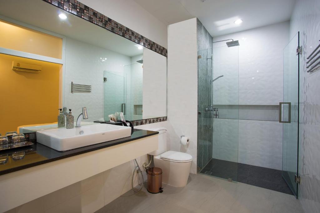 Mūsdienīgs vannas istabas interjers ar stikla dušu, elegantu izlietni un melnu darba virsmu, kas papildina gaišo sienu un siltās krāsas akcentus.