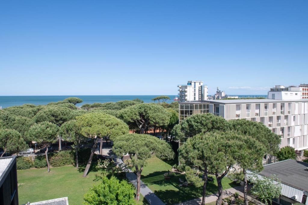 Skats uz jūru, kur redzami zaļi koku vainagi un modernas ēkas. Gaisma ir spilgta, un debesis ir skaidras.