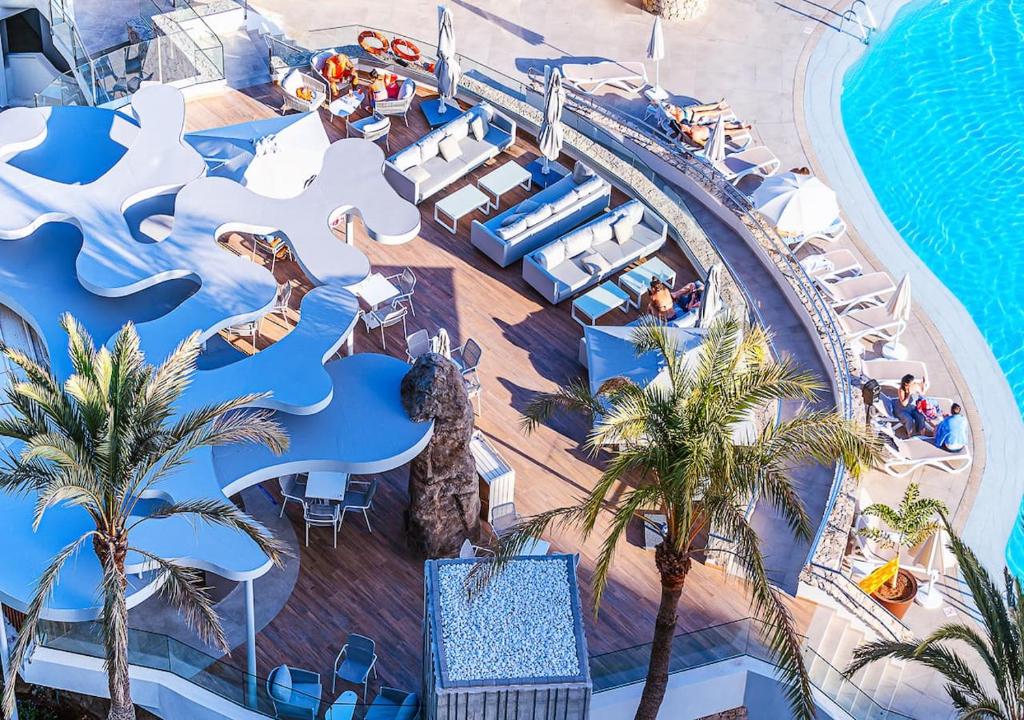 Peldbaseina terase ar modernām mēbelēm un palmām, izveidojot relaksējošu atmosfēru. Skats no augšas uz viesmīlīgu atpūtas vietu pie ūdens.