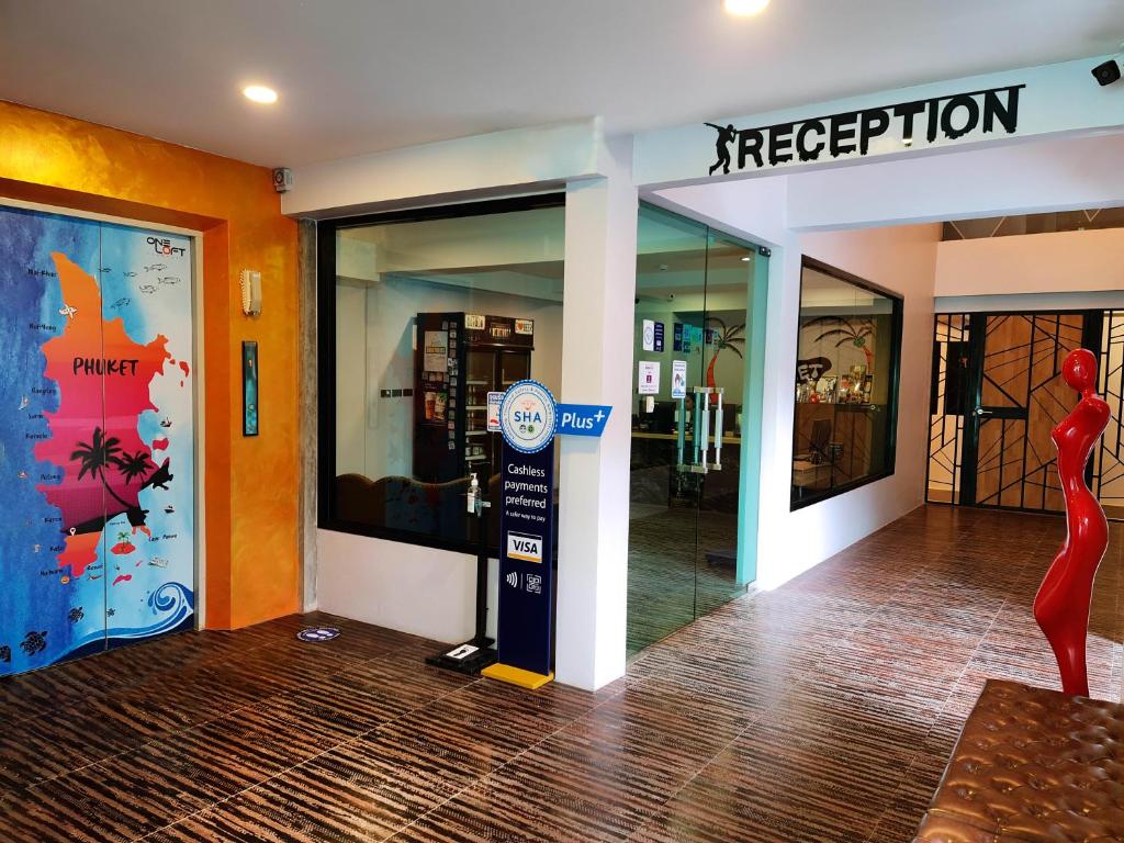 Reģistratūra modernā viesnīcā ar krāsainu Phuket karti uz sienas un stilīgu dekoru. Iekšējā telpa ir gaiša un aicinoša, ar norādēm uz bezskaidras naudas maksājumiem.