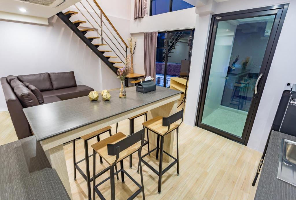 Mūsdienīgs dzīvojamais interjers ar ērtu dīvānu, elegantu galdu un krēsliem, kā arī kāpnēm uz otro stāvu. Lielas loga, kas nodrošina dabisko apgaismojumu un piekļuvi ārējai terasei.