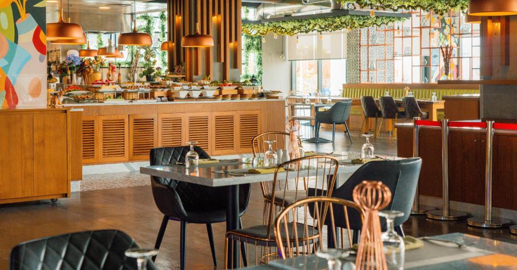 Mūsdienīgs restorāna interjers ar viesējo ēdienu izkārtojumu, koka mēbelēm un elegantu apgaismojumu. Nozares stils apvieno komfortu un estētiku, radot patīkamu atmosfēru.