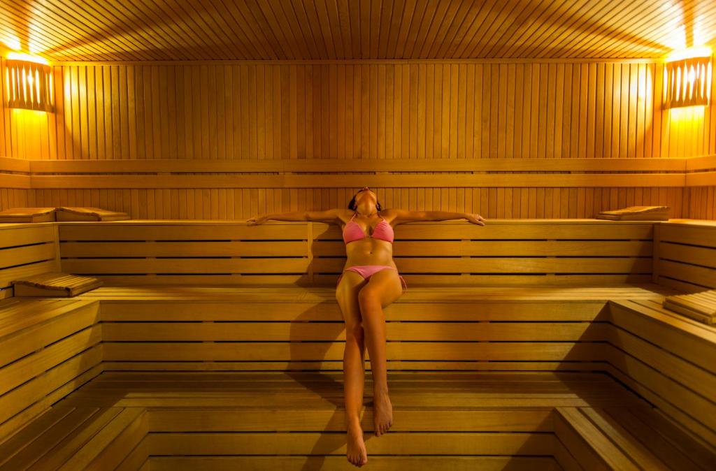 Sieviete rozā peldkostīmā relaksējas koka saunā ar siltu apgaismojumu. Ideāla vide atpūtai un labsajūtai.