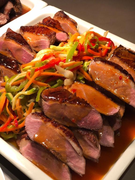 Svaigi pagatavota gaļa ar dārzeņu salātiem un mērci, kas pasniegta uz balta šķīvja. Šis ēdiens ir krāsains un pievilcīgs, piedāvājot brīnišķīgu garšu kombināciju.