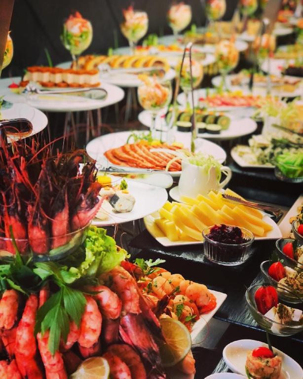 Svaigu jūras produktu un uzkodu bufete, kas ietver garneles, zivis, salātus un dažādas delikateses. Krāsaini pasniegti ēdieni uz galda, radot vilinošu kulinārijas pieredzi.