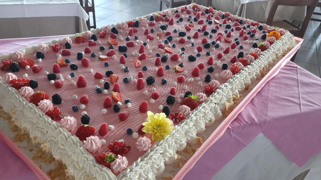 Lielais kūka ar rozā krēmu un dažādiem ogām, rotāta ar krējuma malām un ziediem. Ideāla izvēle svinībām un svinīgiem pasākumiem.