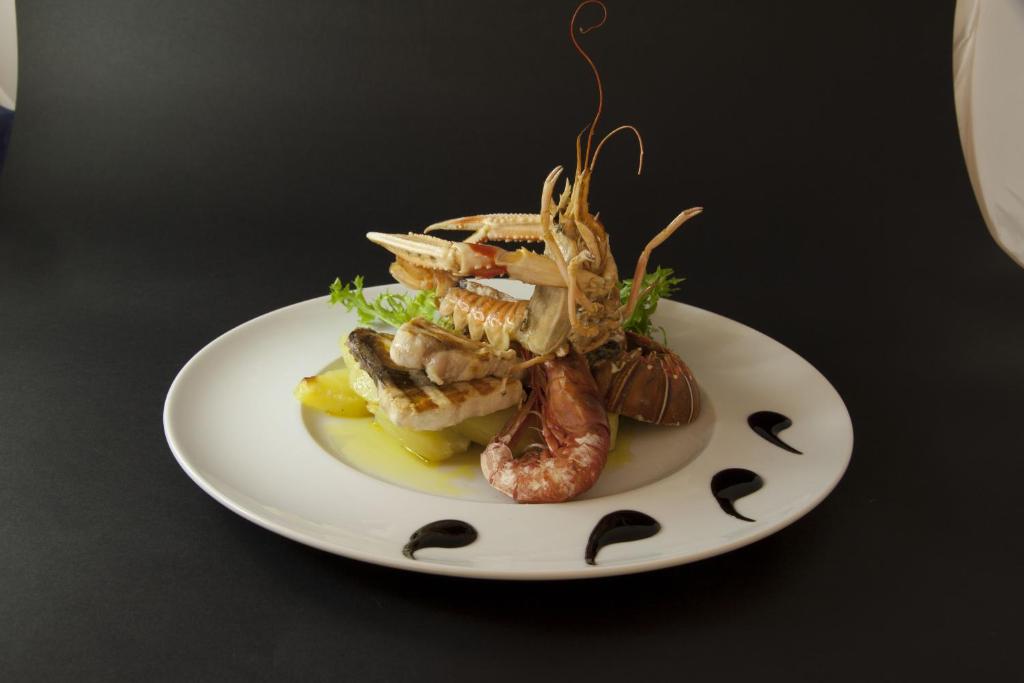 Gurķu un jūras velšu ēdiens, kas pasniegts uz baltas šķīvja ar garnelēm un omāriem, rotāts ar zaļu salātu lapām un dekoratīviem mērces pilieniem.