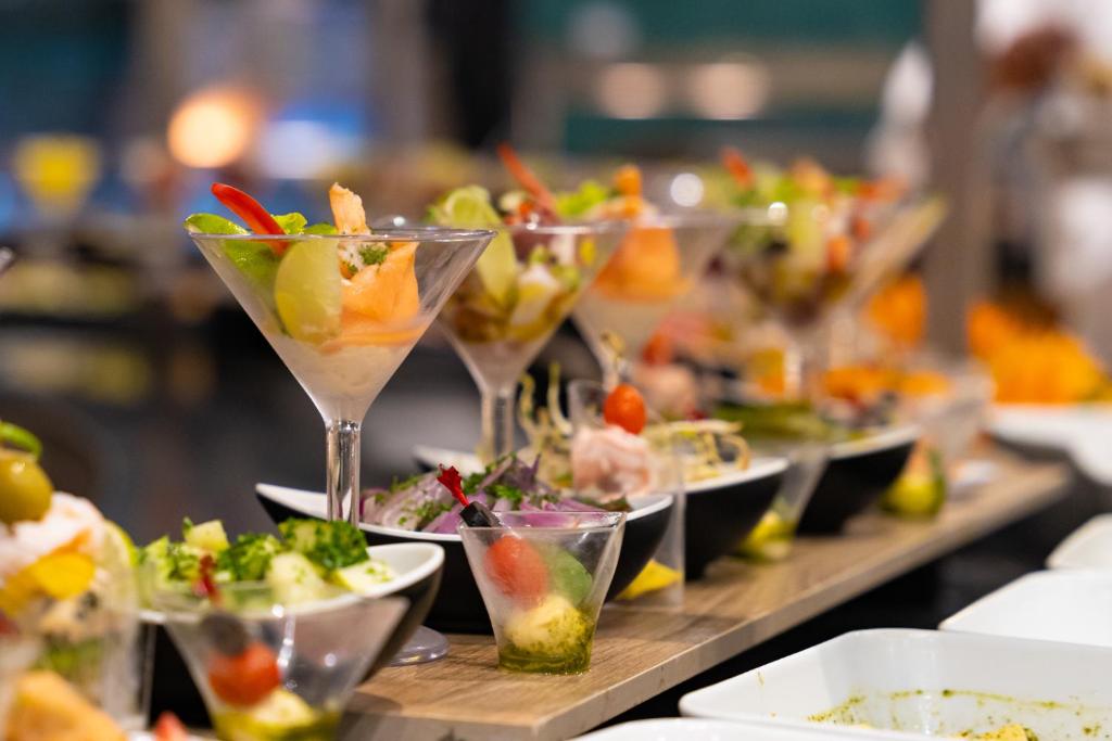 Eleganti pasniegti dažādi jūras veltes un dārzeņu salāti, izkārtoti martini glāzēs un melnās bļodās, radot krāsainu un pievilcīgu uzkodu izvēli.