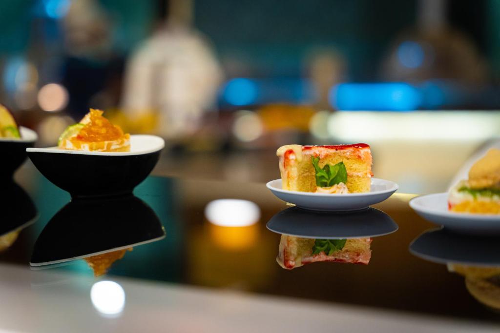 Kompakta deserti uz melna trauka, tostarp krāsains kūka ar zaļu dekorāciju un augļu saldējumu. Reflektējoša virsma piešķir attēlam mūsdienīgu izskatu.