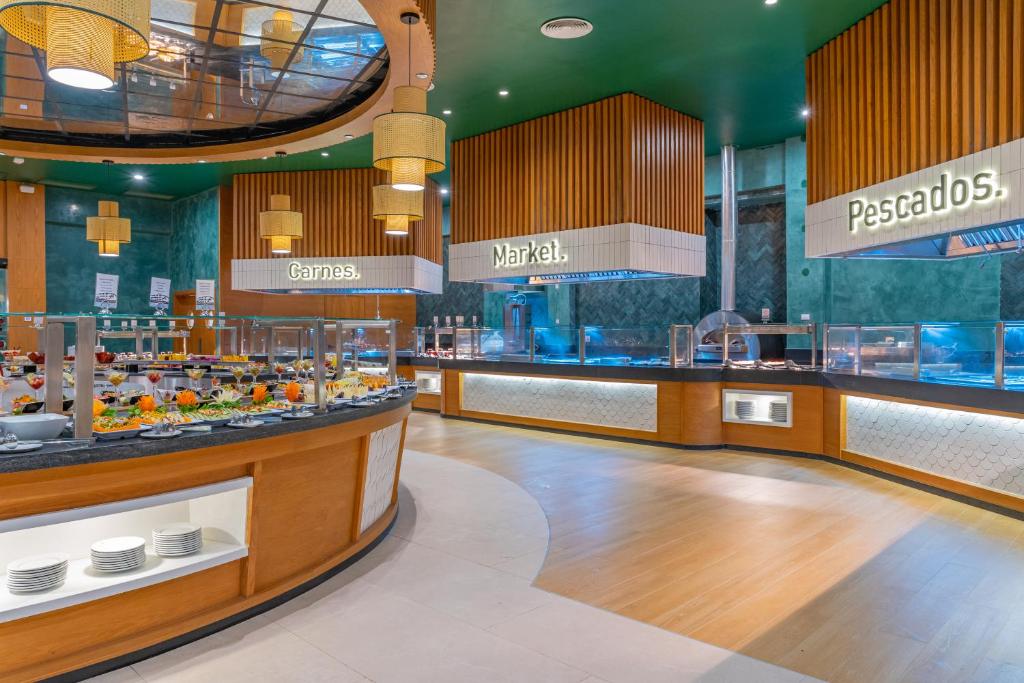 Moderns restorāns ar plašu bufeti, kurā redzami dažādi ēdieni un uzraksti 