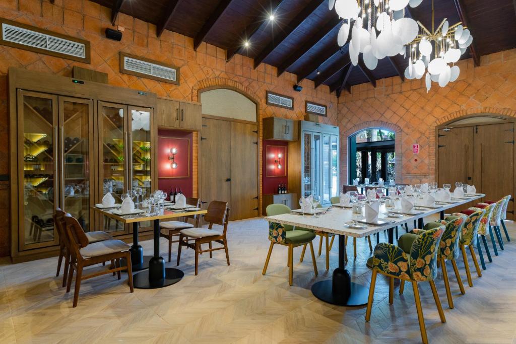 Eleganti iekārtota restorāna iekšiene ar koka griestiem un modernu apgaismojumu, kurā redzami galdi ar galda piederumiem un krēslus ar krāsainiem audumiem. Restorānā ir arī vīna glabāšanas skapji un liels logs, kas piedāvā skatu uz āru.